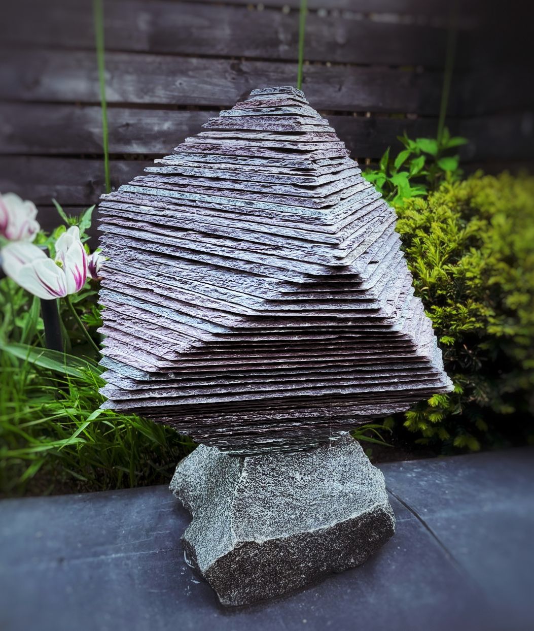 Abstract geometric sculpture made from layered roof slate, forming a cube-like shape with a diagonal opening.